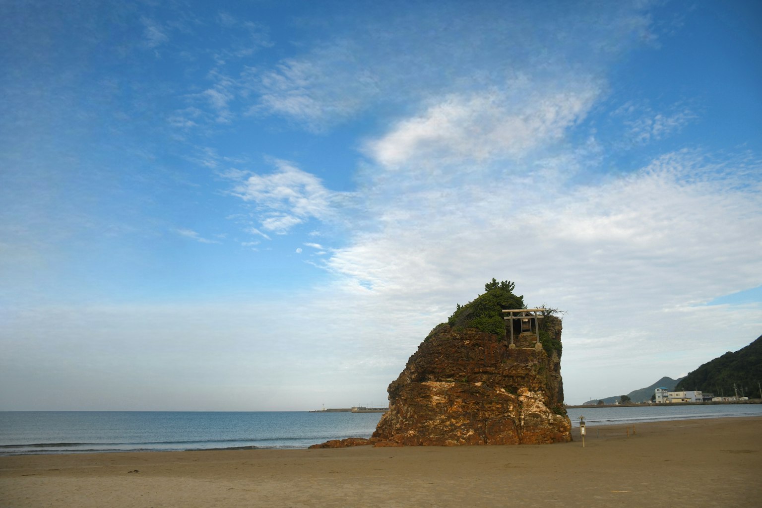 Une formation rocheuse avec de la verdure sur une plage sous un ciel bleu