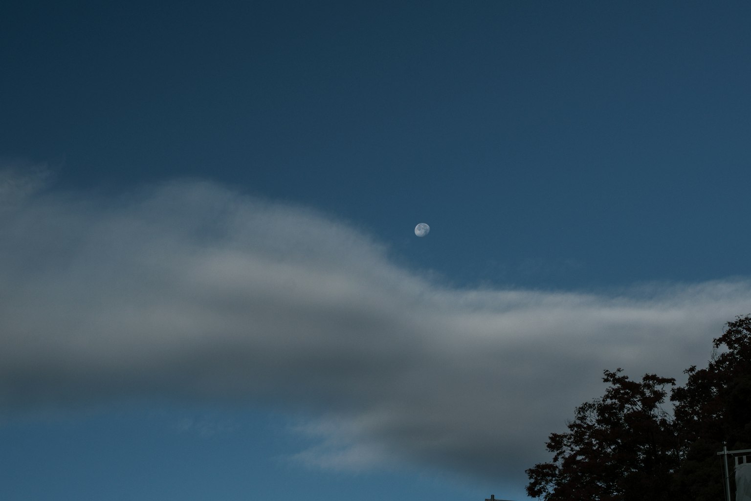 Una vista de la luna asomando entre nubes en un cielo azul