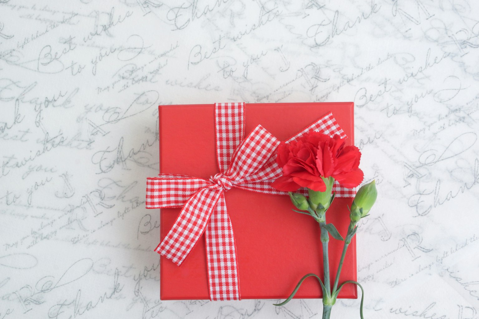A red gift box with a checkered ribbon and a red carnation flower
