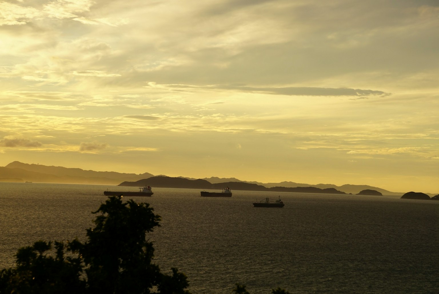 Navi cargo sull'oceano con isole sullo sfondo durante il tramonto