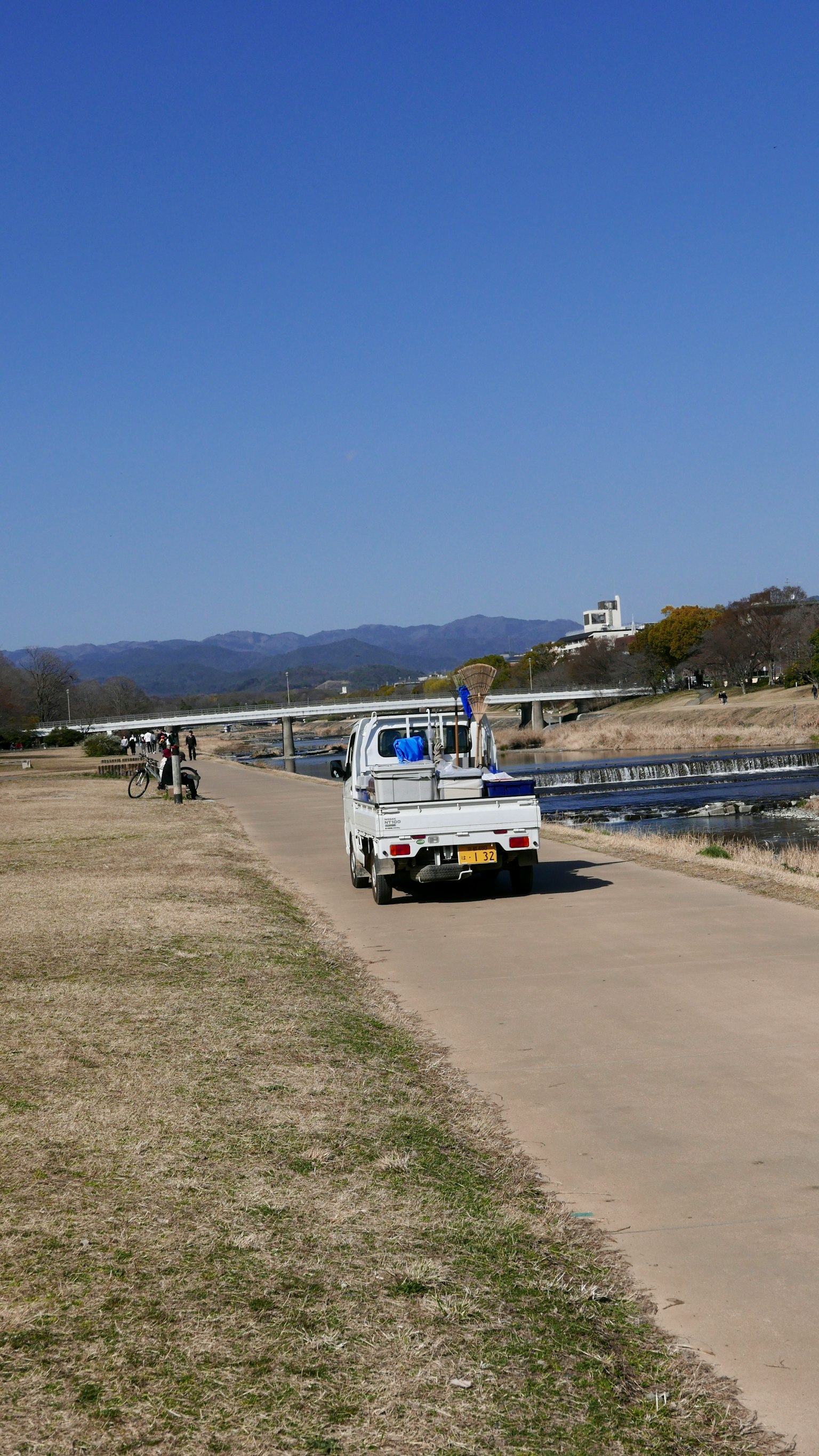 Small truck driving along a riverside path under a blue sky