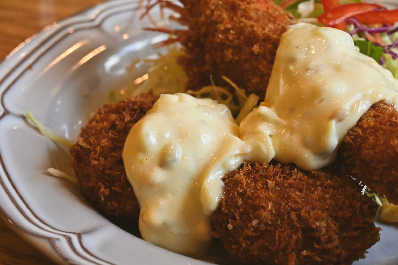 Piatto di crocchette fritte croccanti guarnite con salsa cremosa e accompagnate da insalata
