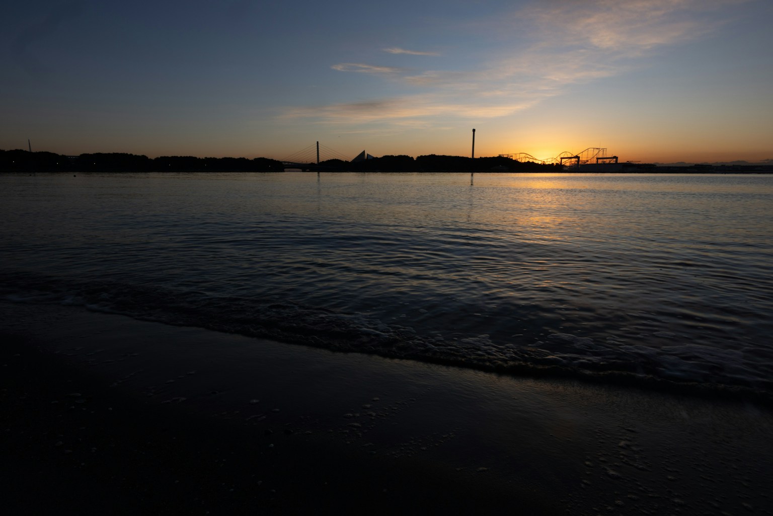 Sunset over calm sea with silhouettes of distant hills