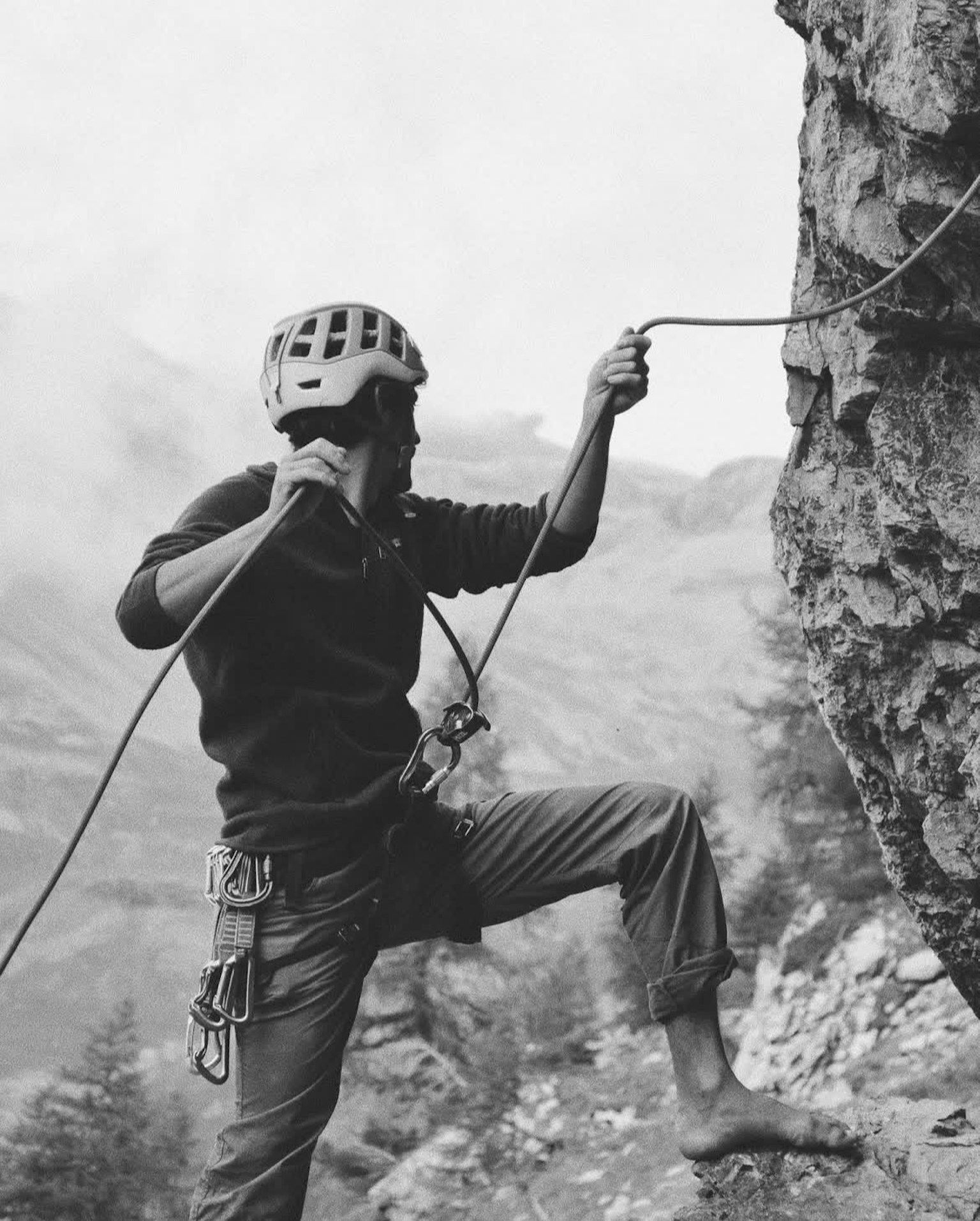Black and white photo of a climber ascending a rock wearing a helmet and holding a rope