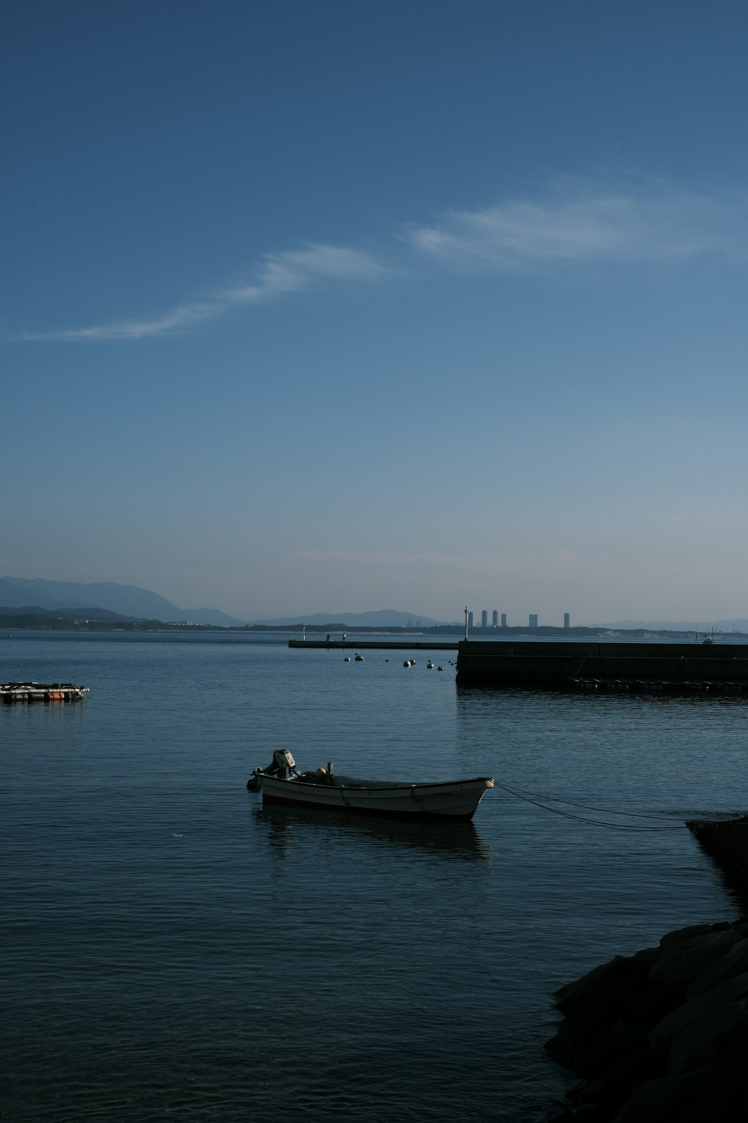 一只小船漂浮在平静的水面上，远处是港口