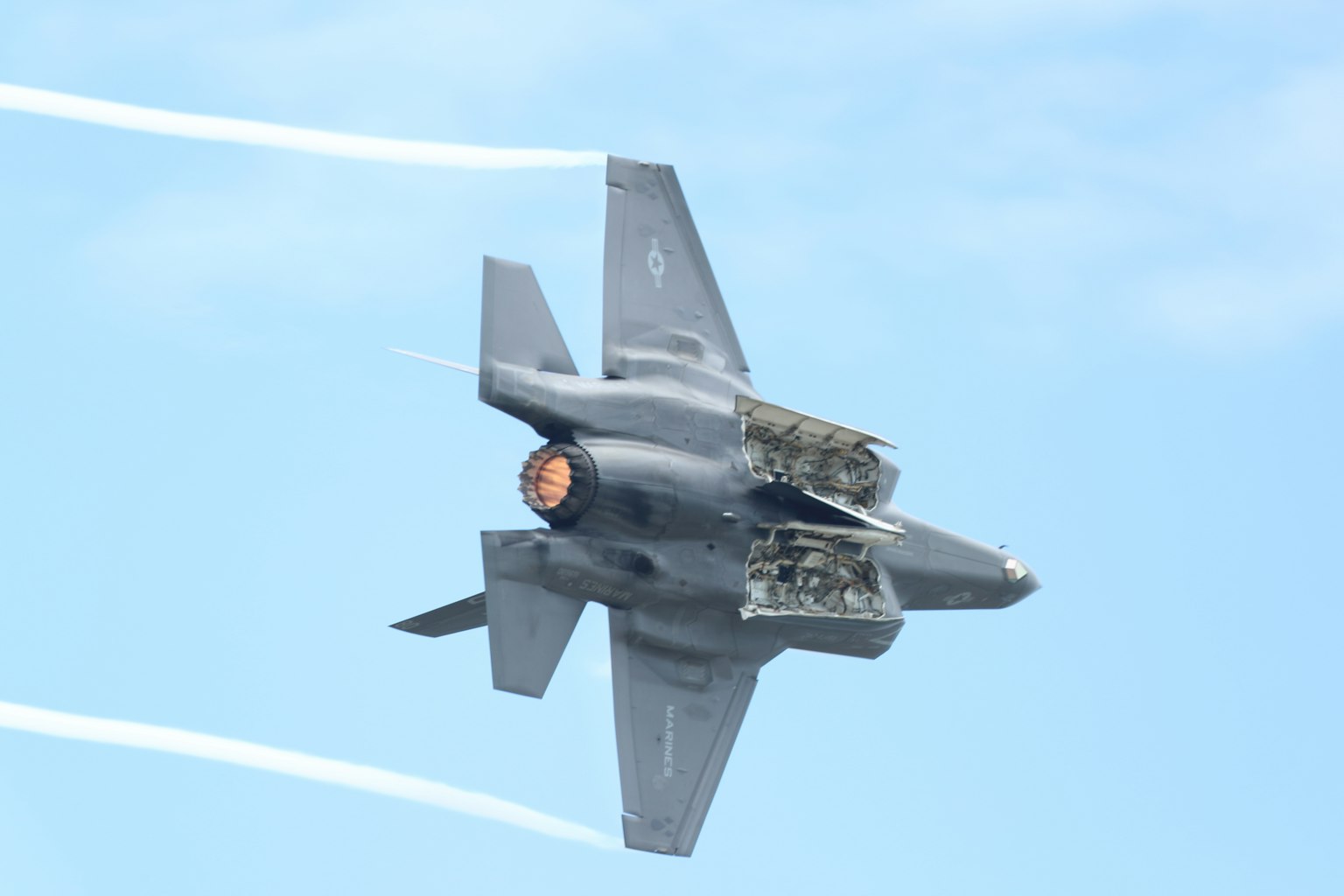F-35 fighter jet performing a maneuver in the sky with exposed engine section