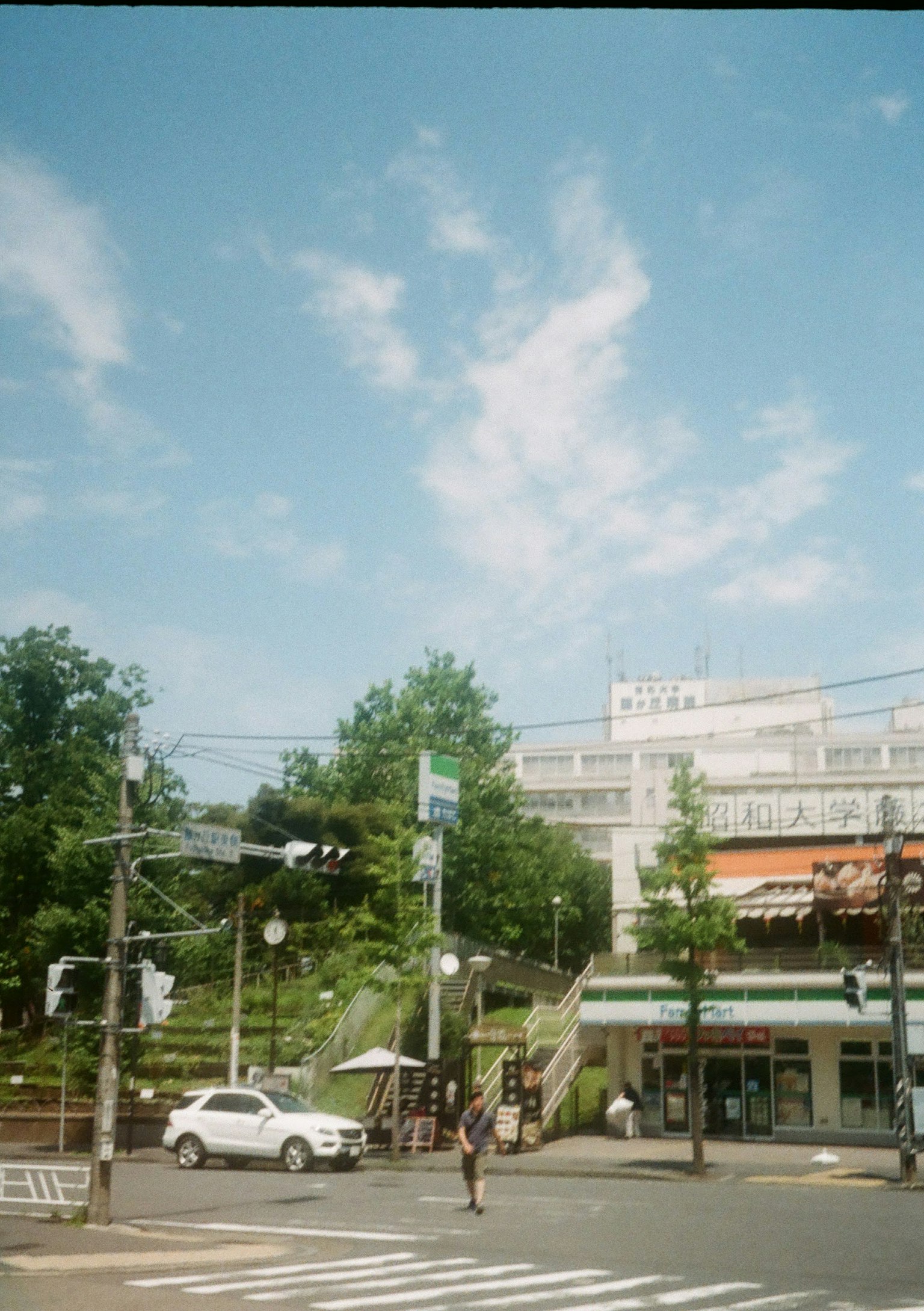 街角场景，蓝天和云朵 交叉口站着的人 可见的汽车和绿色树木