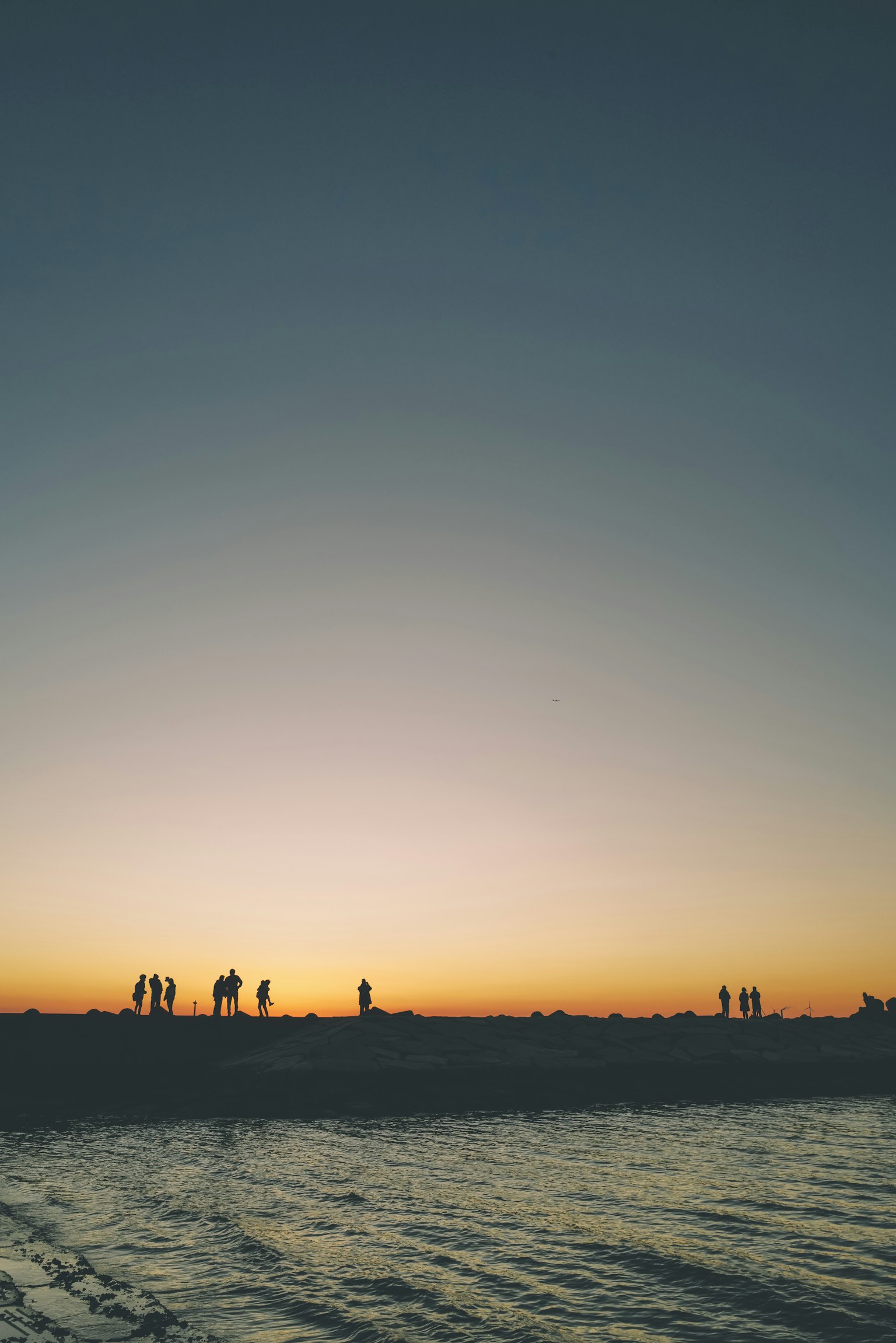 Silhouetten von Menschen an einem Strand bei Sonnenuntergang mit ruhigem Wasser