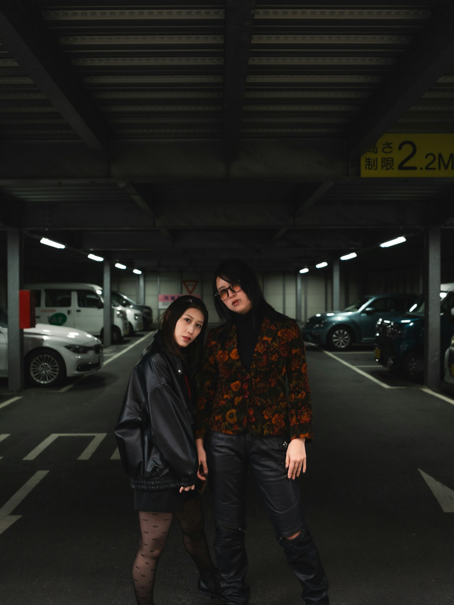 两名女性在停车场摆姿势穿着黑色夹克和花卉图案的上衣明亮的灯光和背景中的汽车