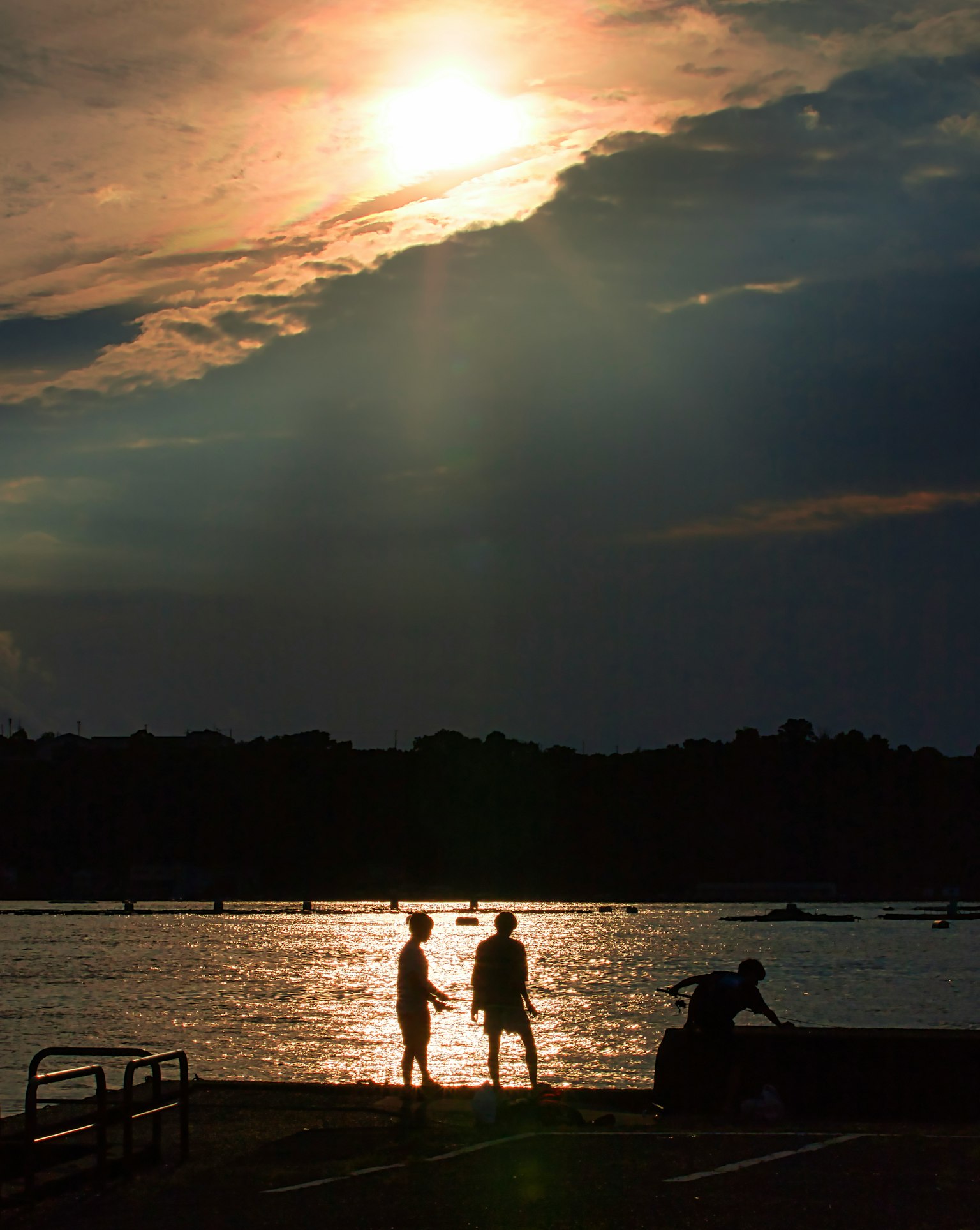 Silhouette von zwei Personen am Ufer des Sees bei Sonnenuntergang mit glitzerndem Wasser