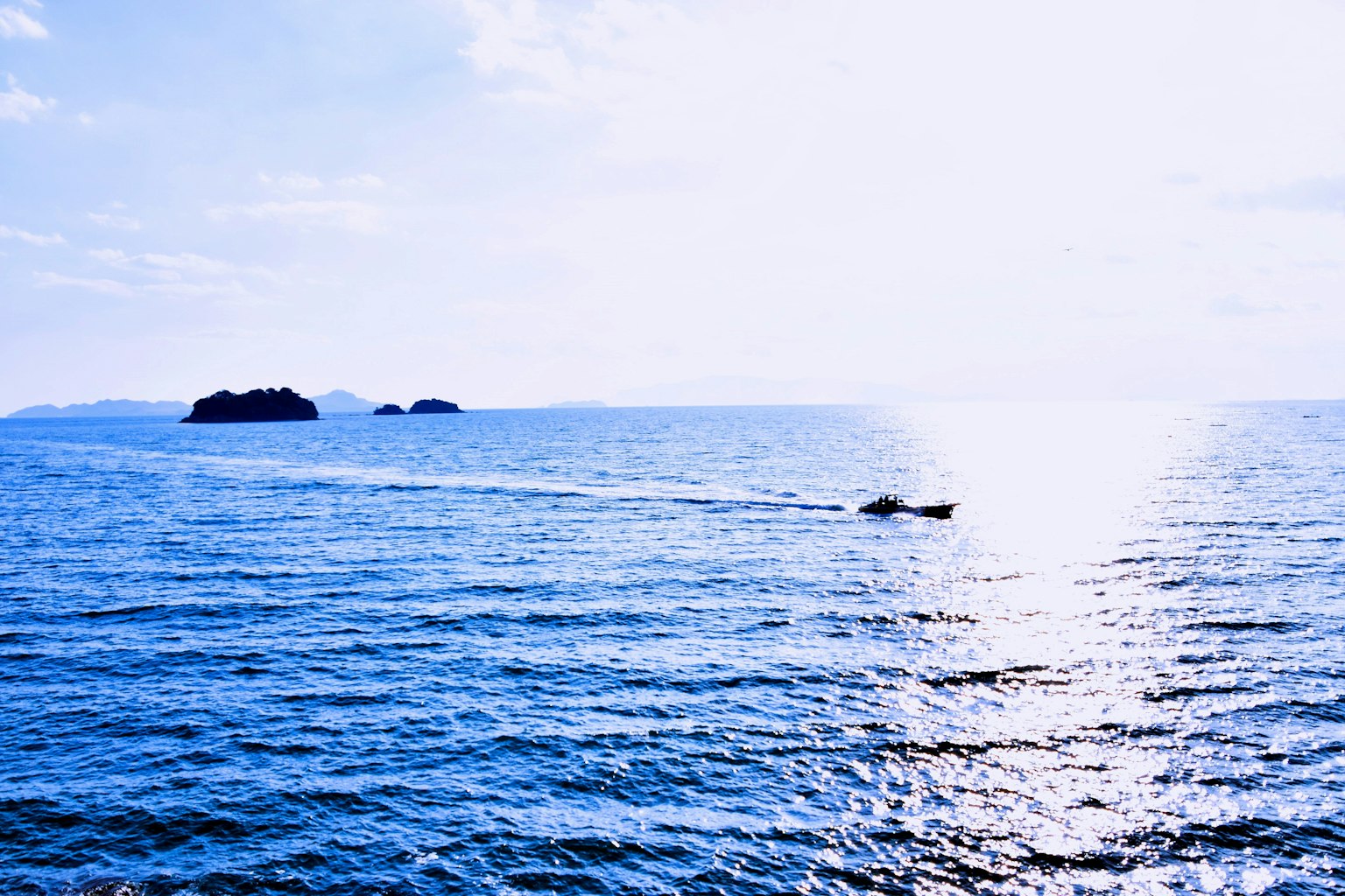 A scenic view of blue ocean with small islands and a boat moving