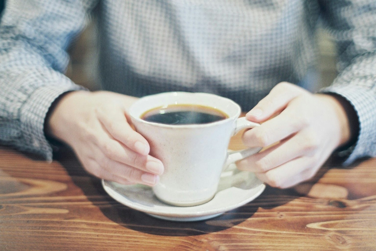 มือที่ถือถ้วยกาแฟสีขาวที่มีกาแฟดำ