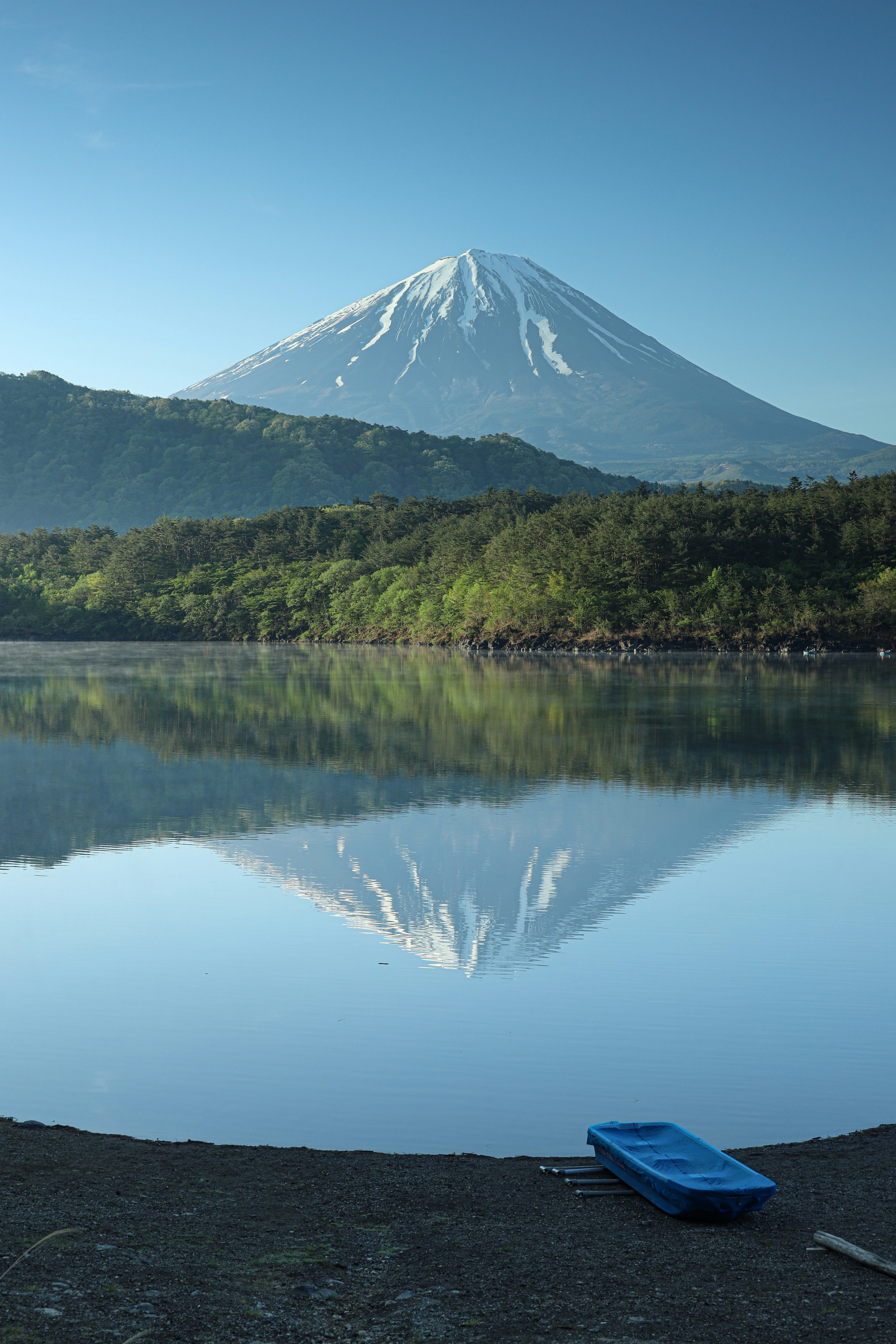Scorcio sulle rive del lago Saiko con la riflessione del Monte Fuji e una barca blu