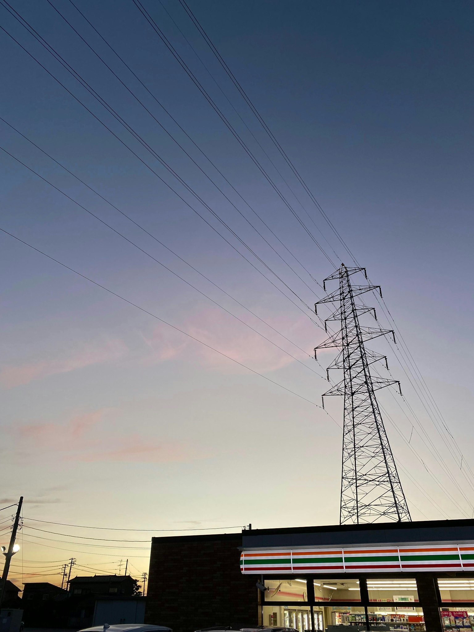 Stromleitungen vor einem bunten Sonnenuntergangshimmel mit einem Geschäft im Vordergrund
