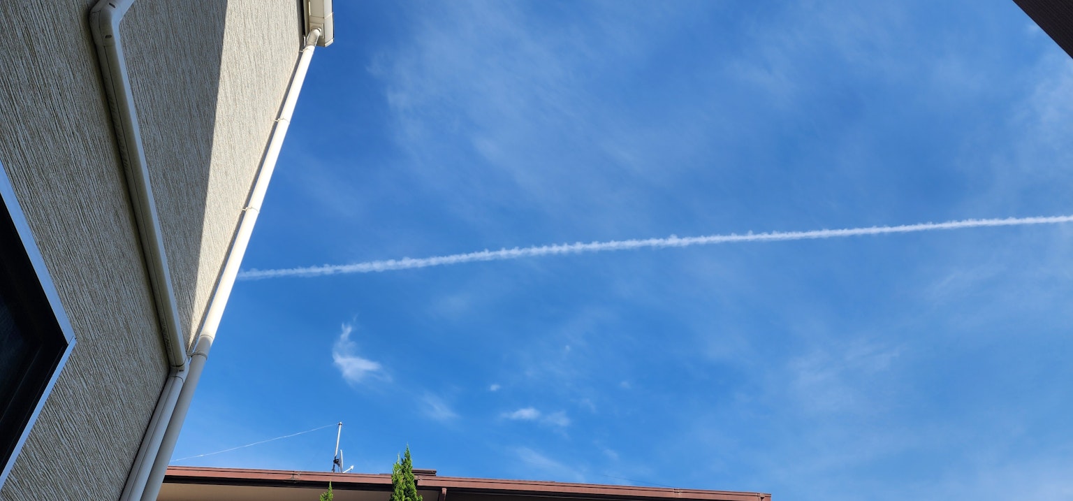 Un cielo blu chiaro con una scia bianca sopra un'area residenziale