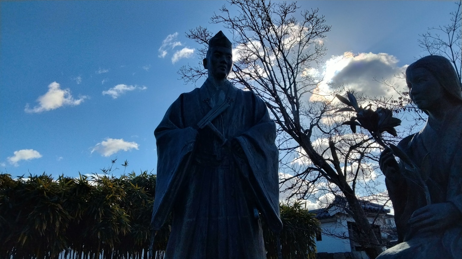 Statue under a blue sky featuring intricate details and surrounding foliage