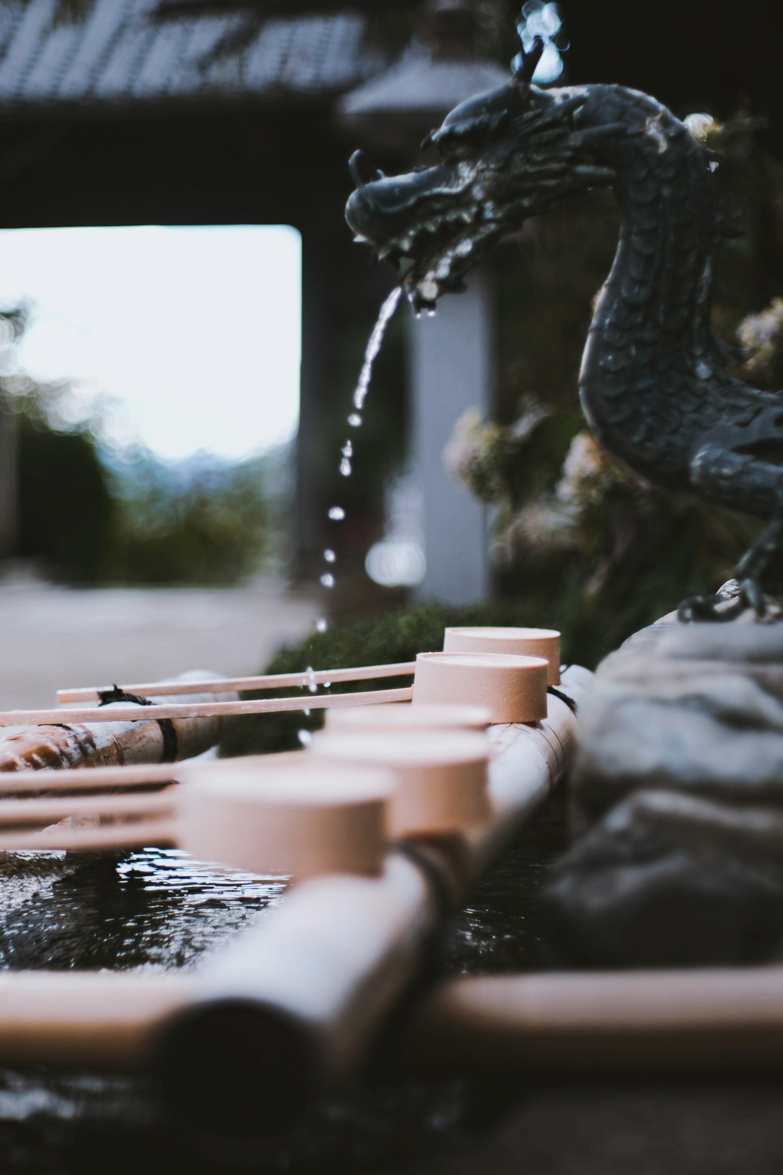 Japanischer Garten mit einer Drachen-Skulptur, die Wasser spritzt, und Bambusbecken