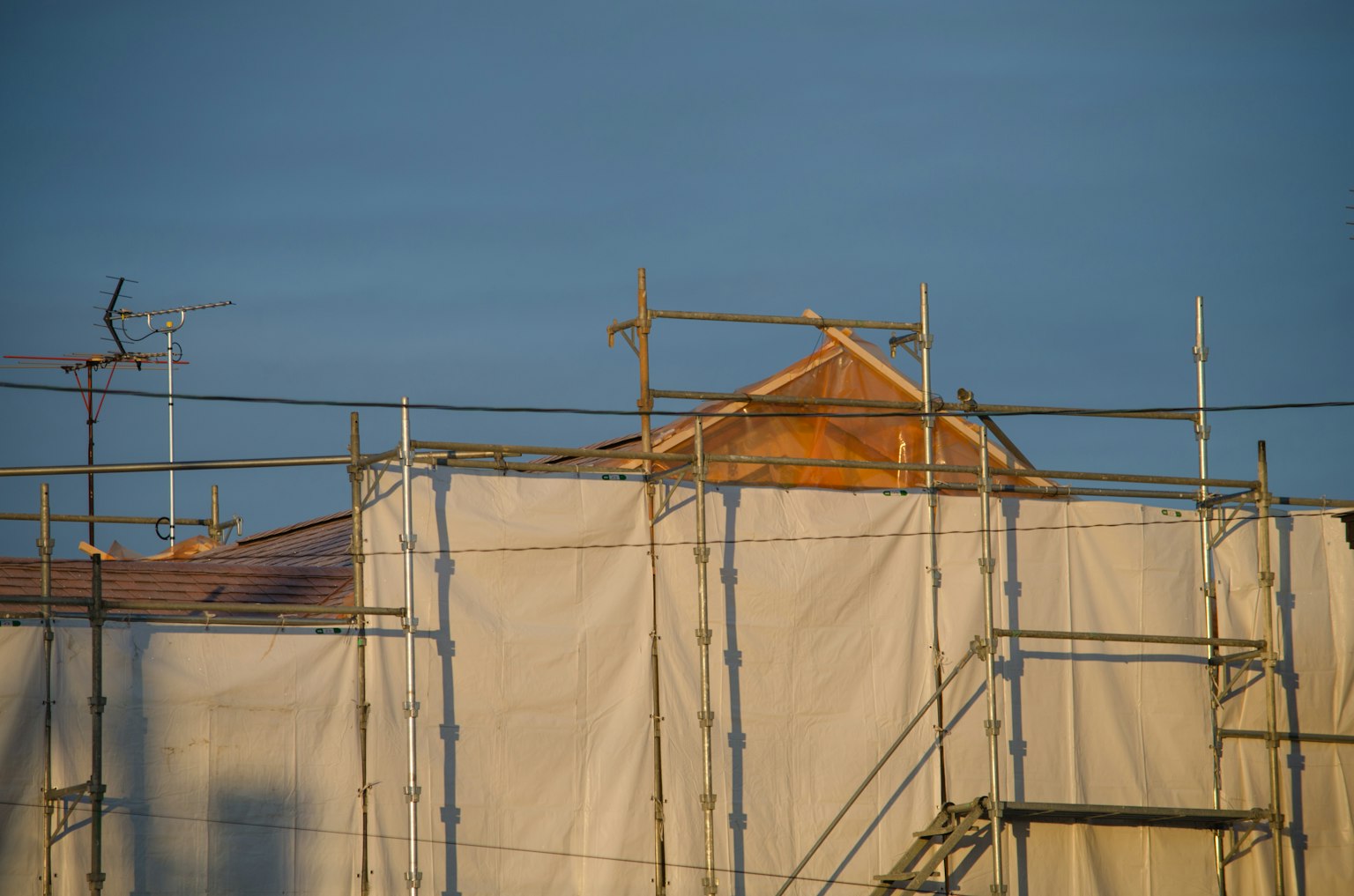 Échafaudage et bâche blanche couvrant une maison en construction avec un toit visible