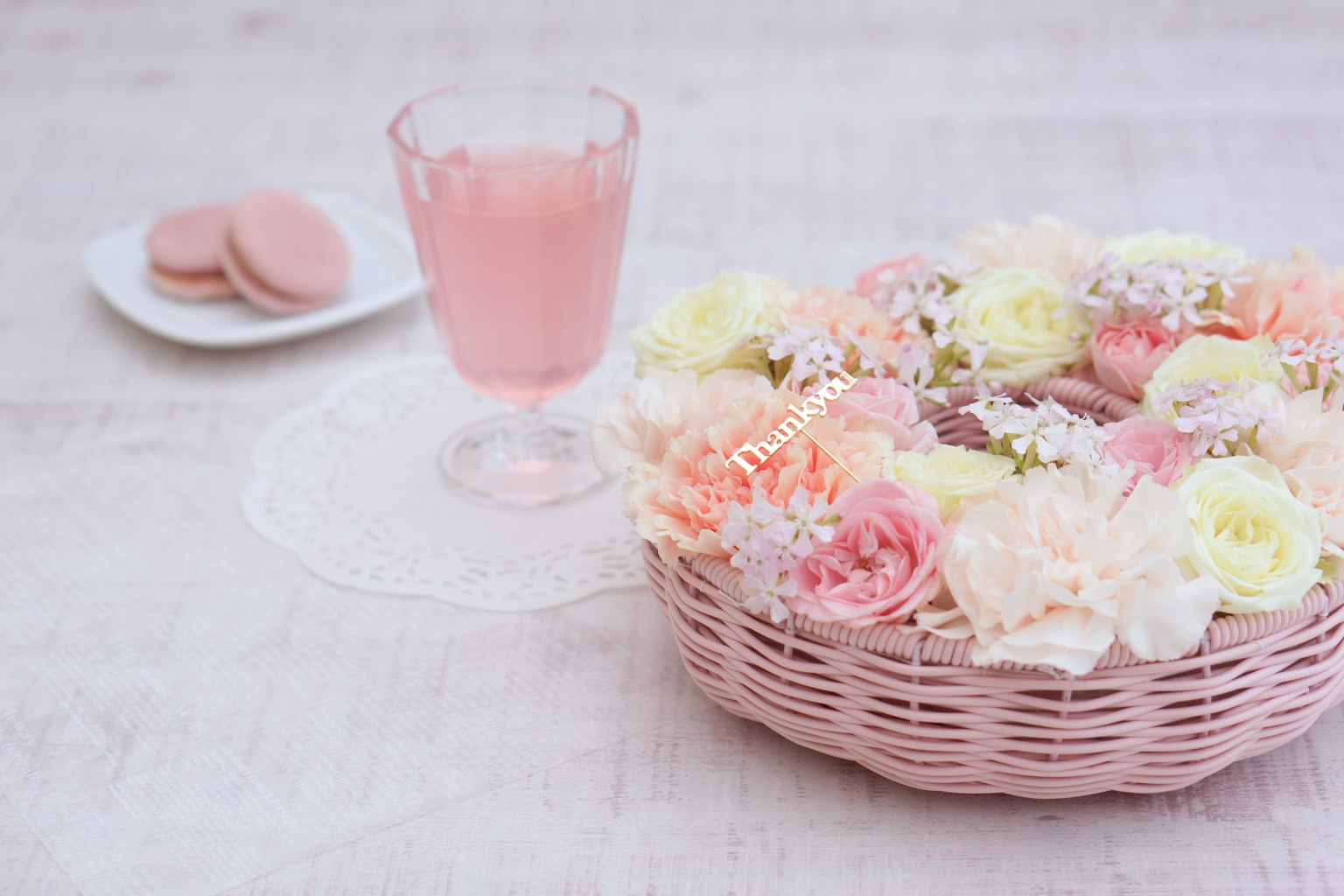Sebuah keranjang bunga pink dan segelas minuman pink di atas meja