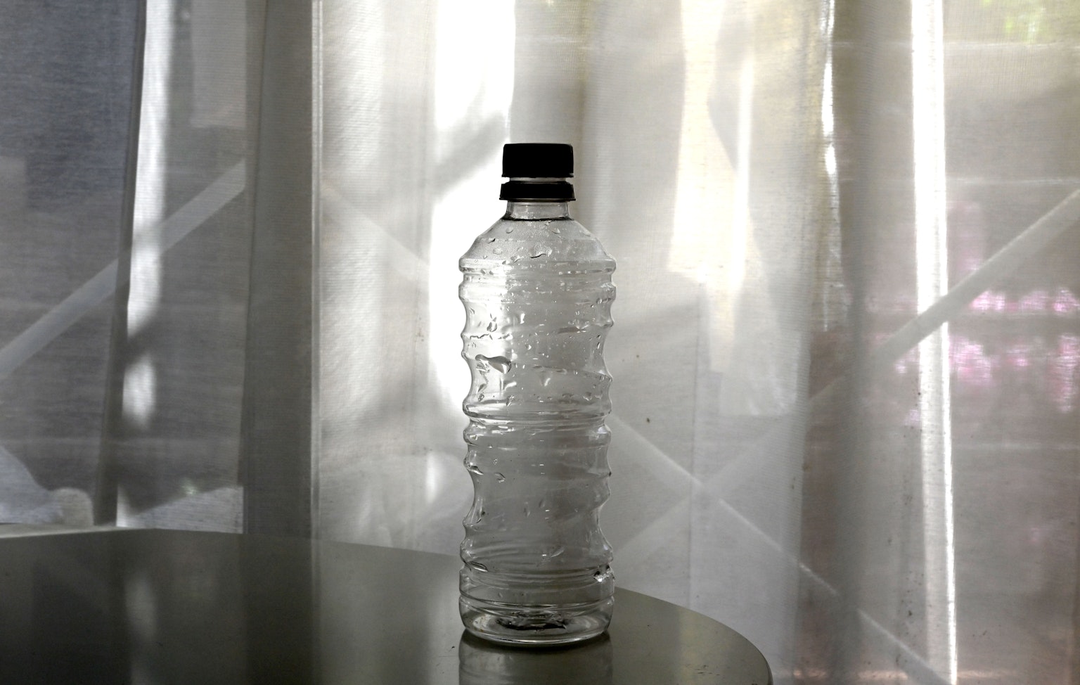Una bottiglia d'acqua trasparente posizionata davanti a tende bianche