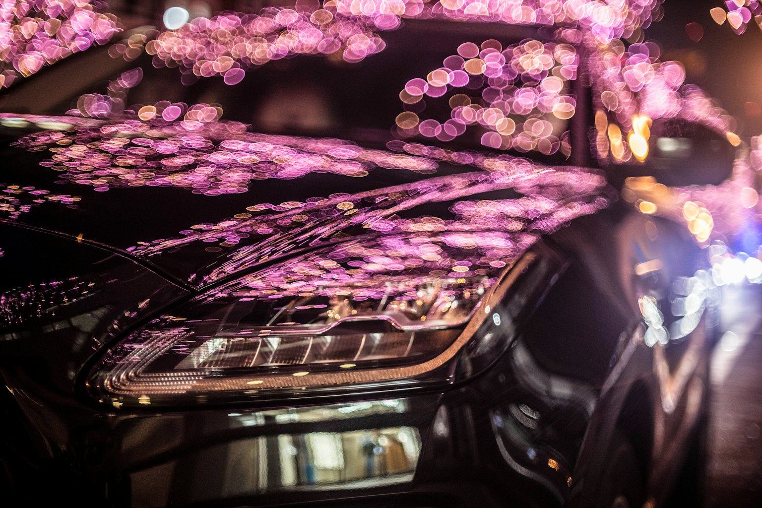 Gros plan d'une voiture noire réfléchissant des lumières bokeh violettes la nuit