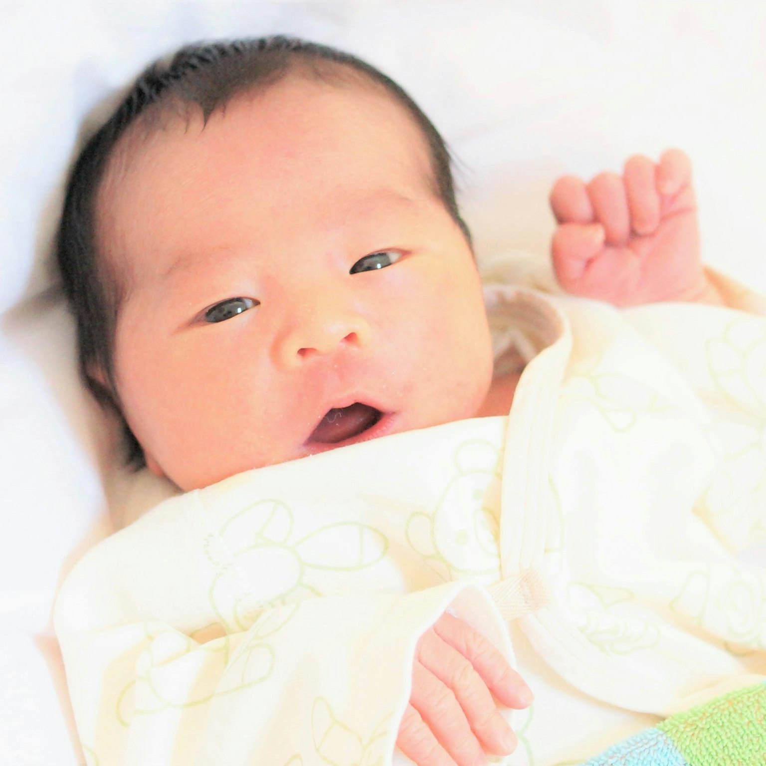 a baby lying on a white blanket with open eyes