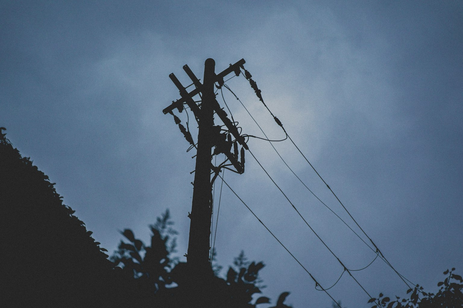 Silhouette eines Strommasts und Kabels unter einem dunklen Himmel
