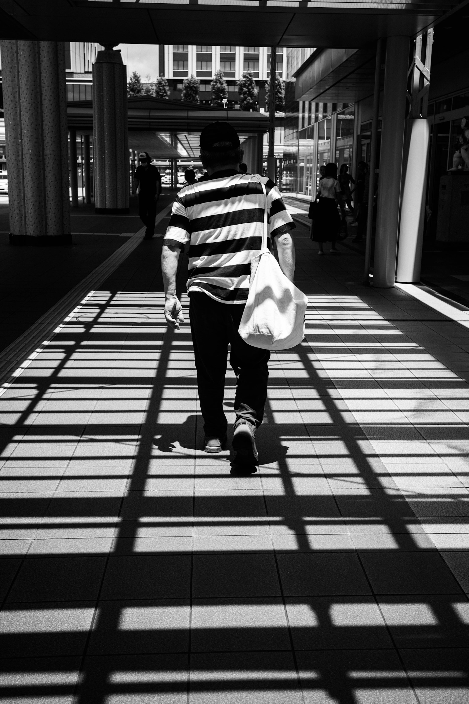 Una persona in una maglietta a righe bianche e nere che cammina con una borsa Ombre proiettate sul pavimento
