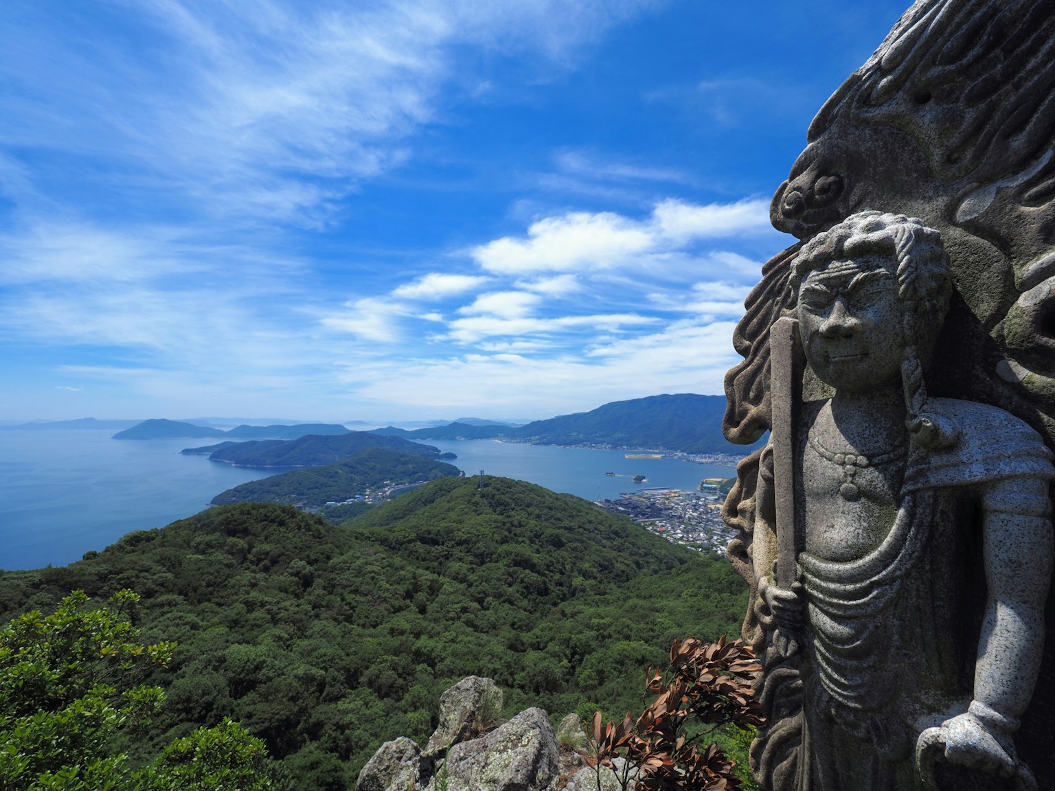 Statue de Bouddha surplombant un océan bleu et des montagnes verdoyantes