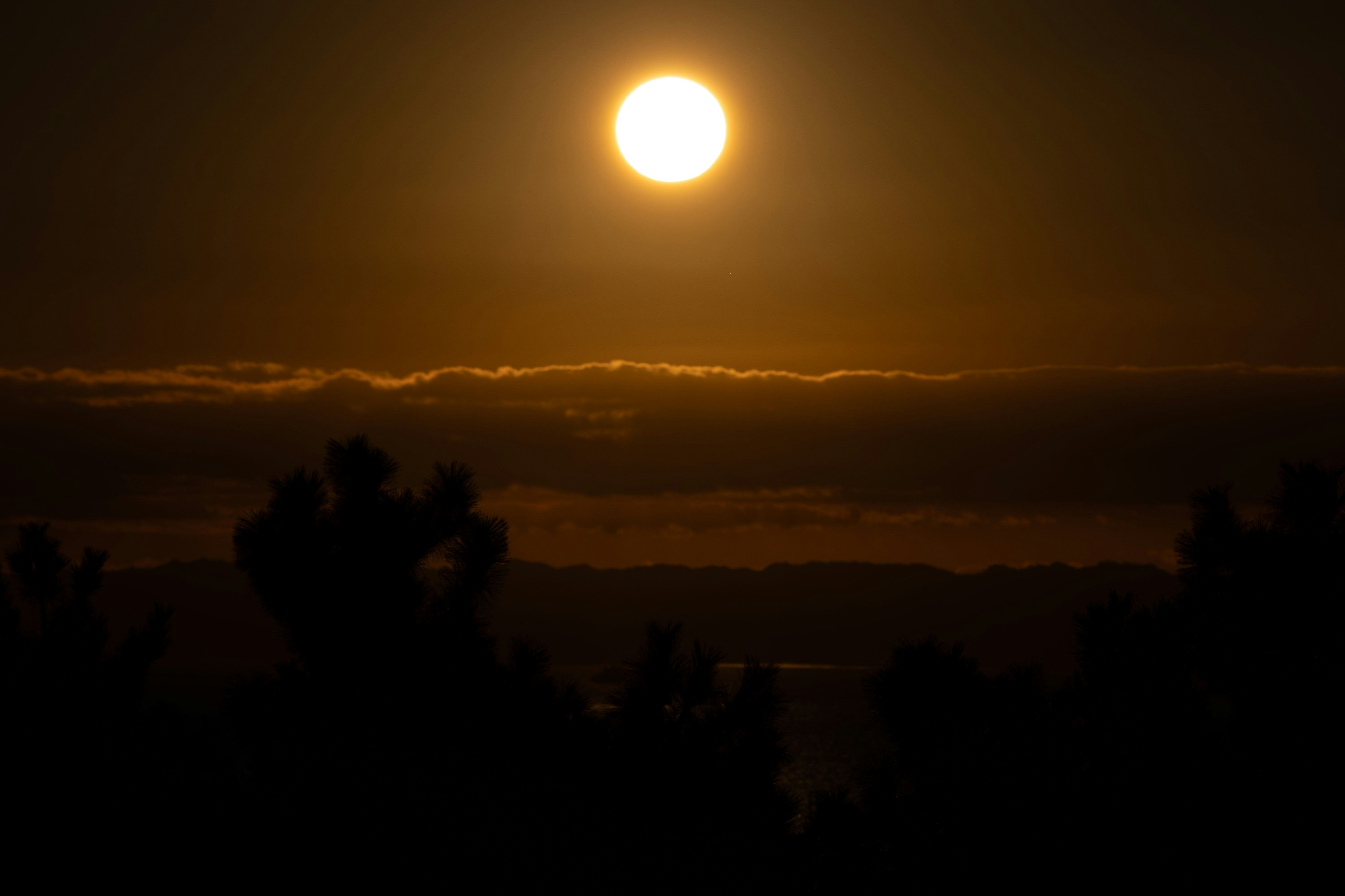 夕暮れの空に浮かぶ月明かりのような光と雲のシルエット