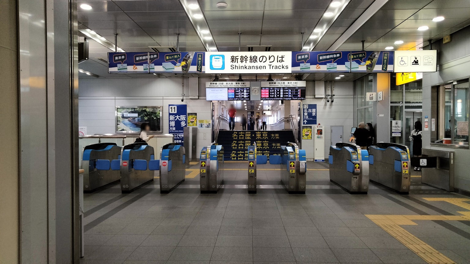 ภาพมุมมองของประตูสถานีรถไฟที่มีเครื่องกั้นตั๋วสีเงินและป้าย