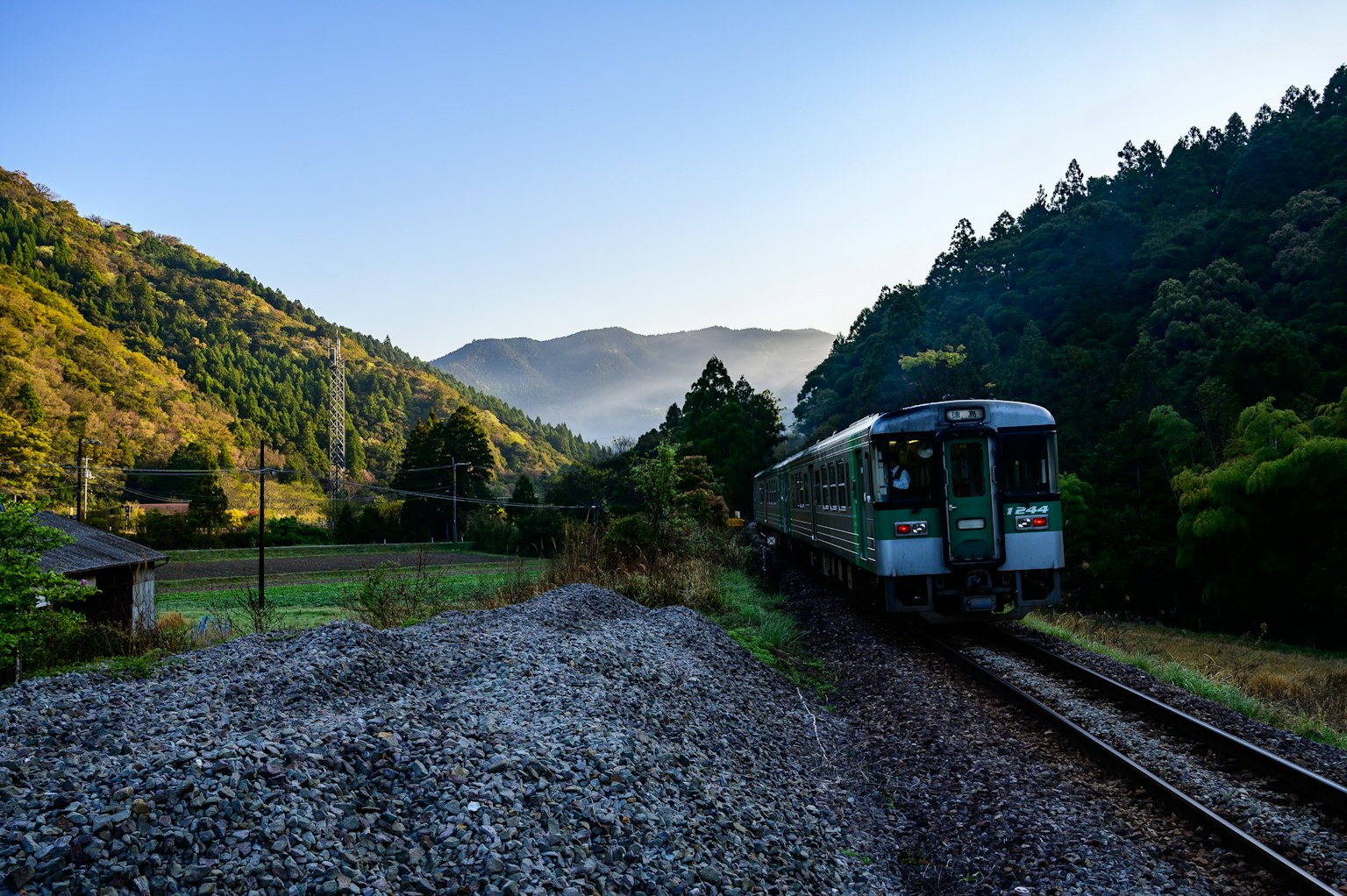 Treno verde che attraversa un paesaggio montano con nebbia mattutina