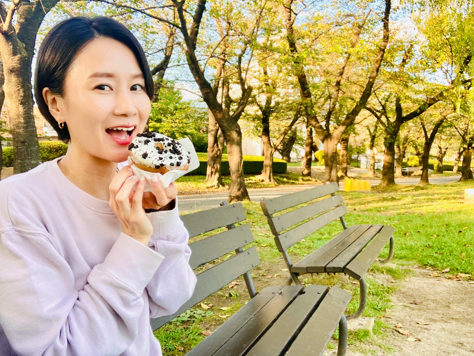 Woman enjoying a dessert in a park with green grass and trees in the background