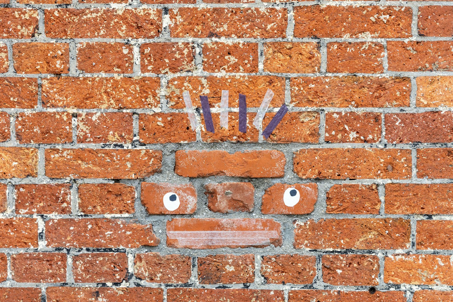 レンガの壁に描かれたユニークな顔のアート作品目を引く目と口が特徴