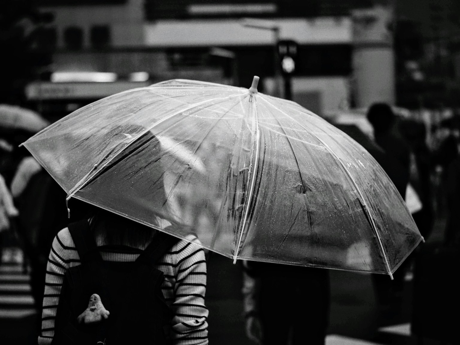 Une personne tenant un parapluie transparent au milieu d'une foule en noir et blanc