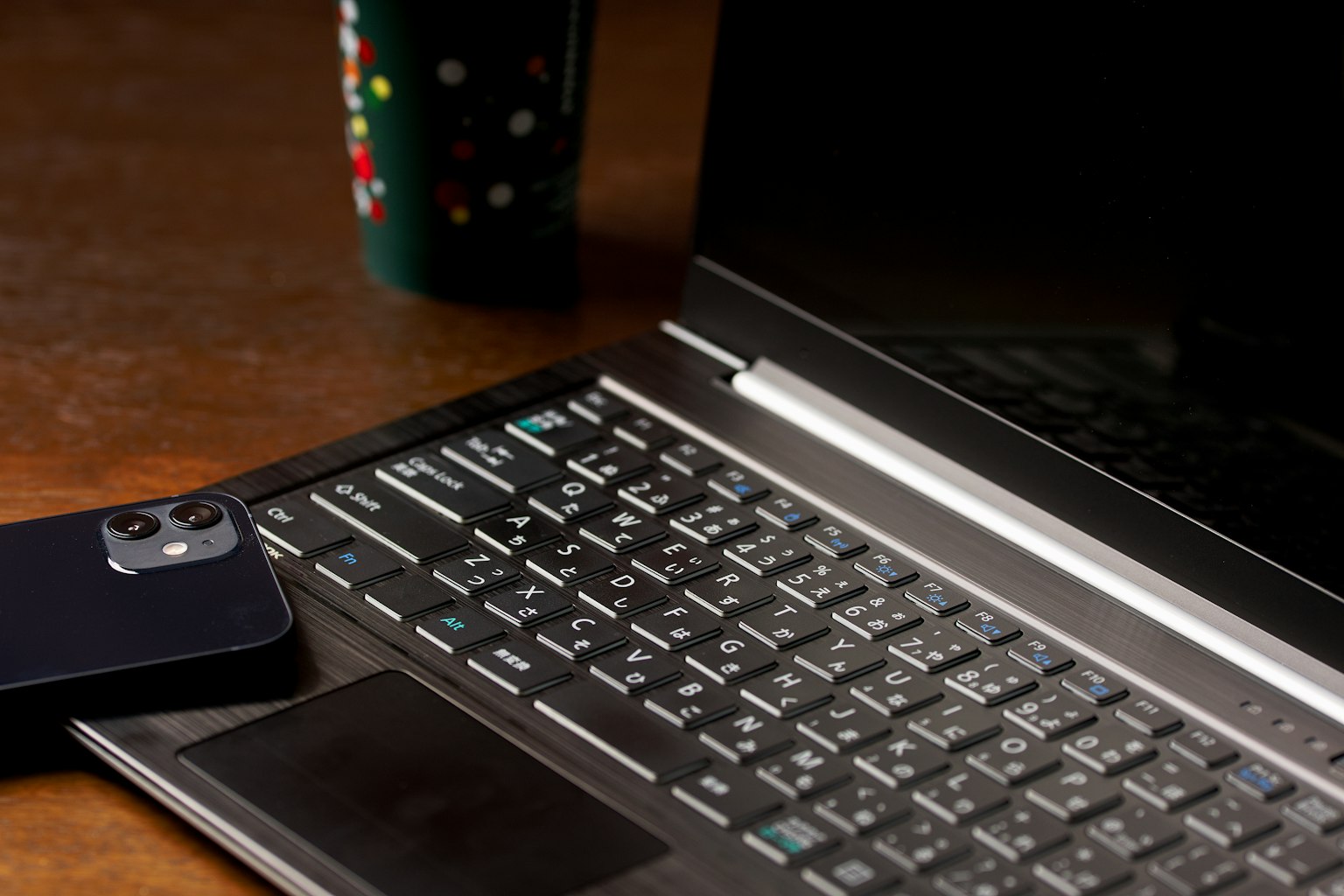 Primo piano di una tastiera di laptop e uno smartphone su un tavolo di legno