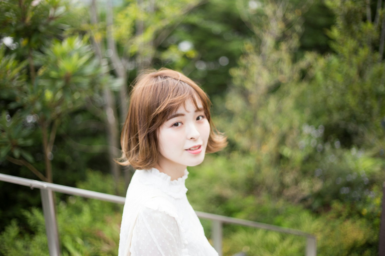 녹색 배경 앞에 서 있는 여성의 초상 화이트 블라우스를 입고 짧은 머리를 한 젊은 여성