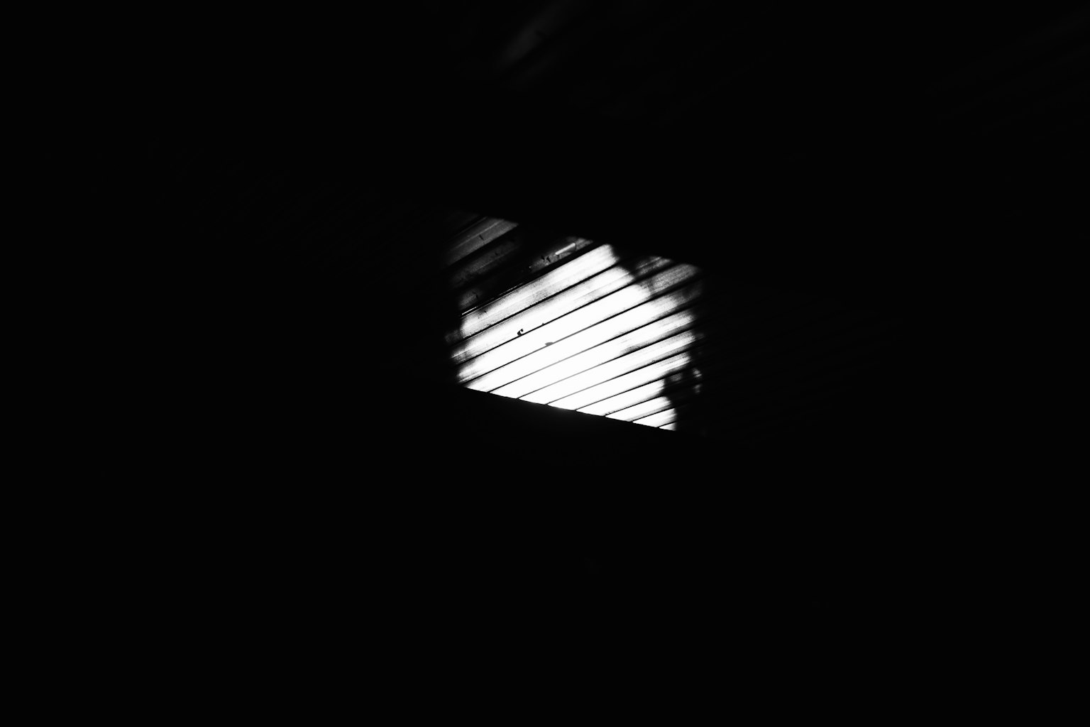 Une fenêtre avec des lamelles projetant de la lumière dans un espace sombre