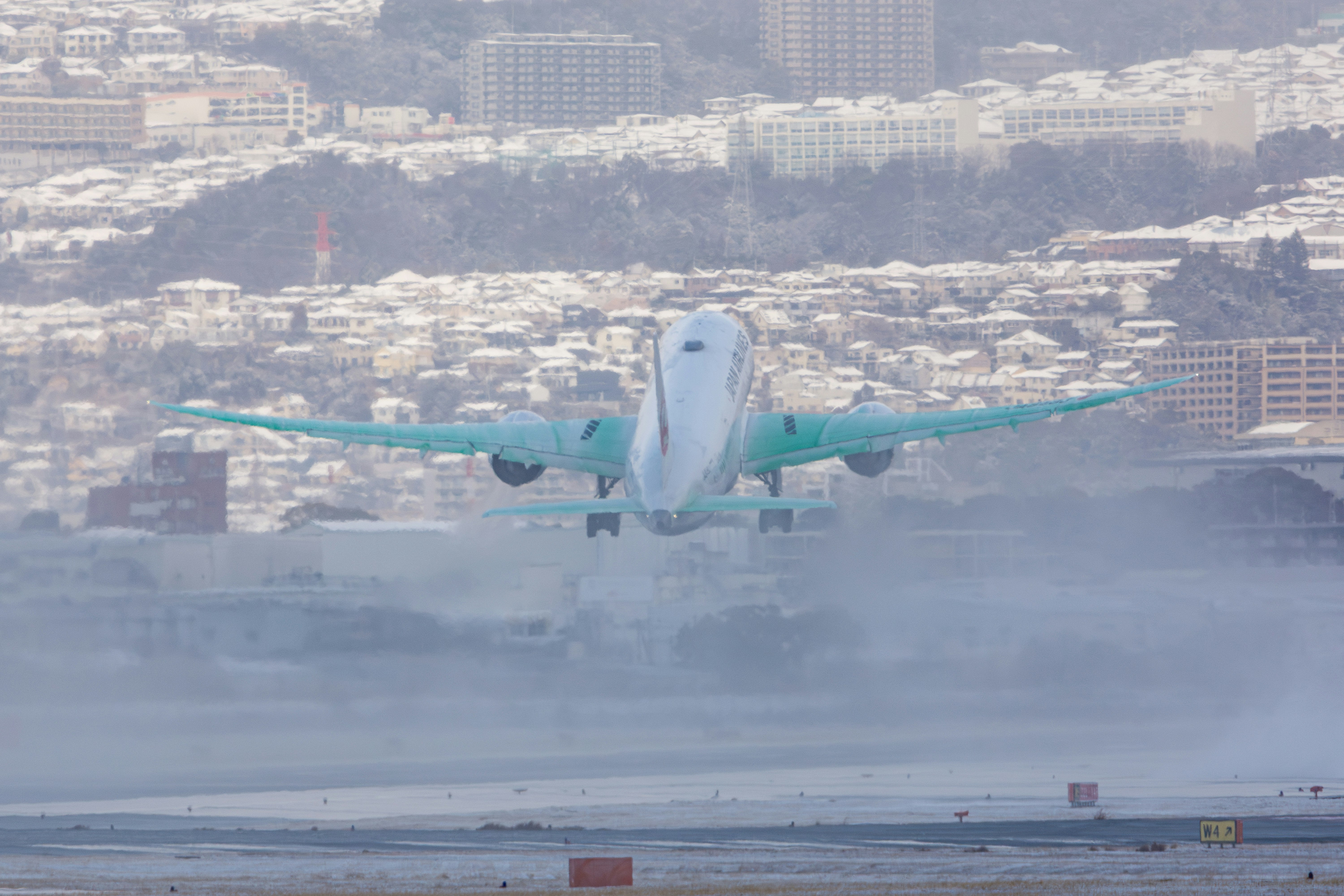 雪煙の中を離陸する飛行機の翼に散布された凍結防止剤