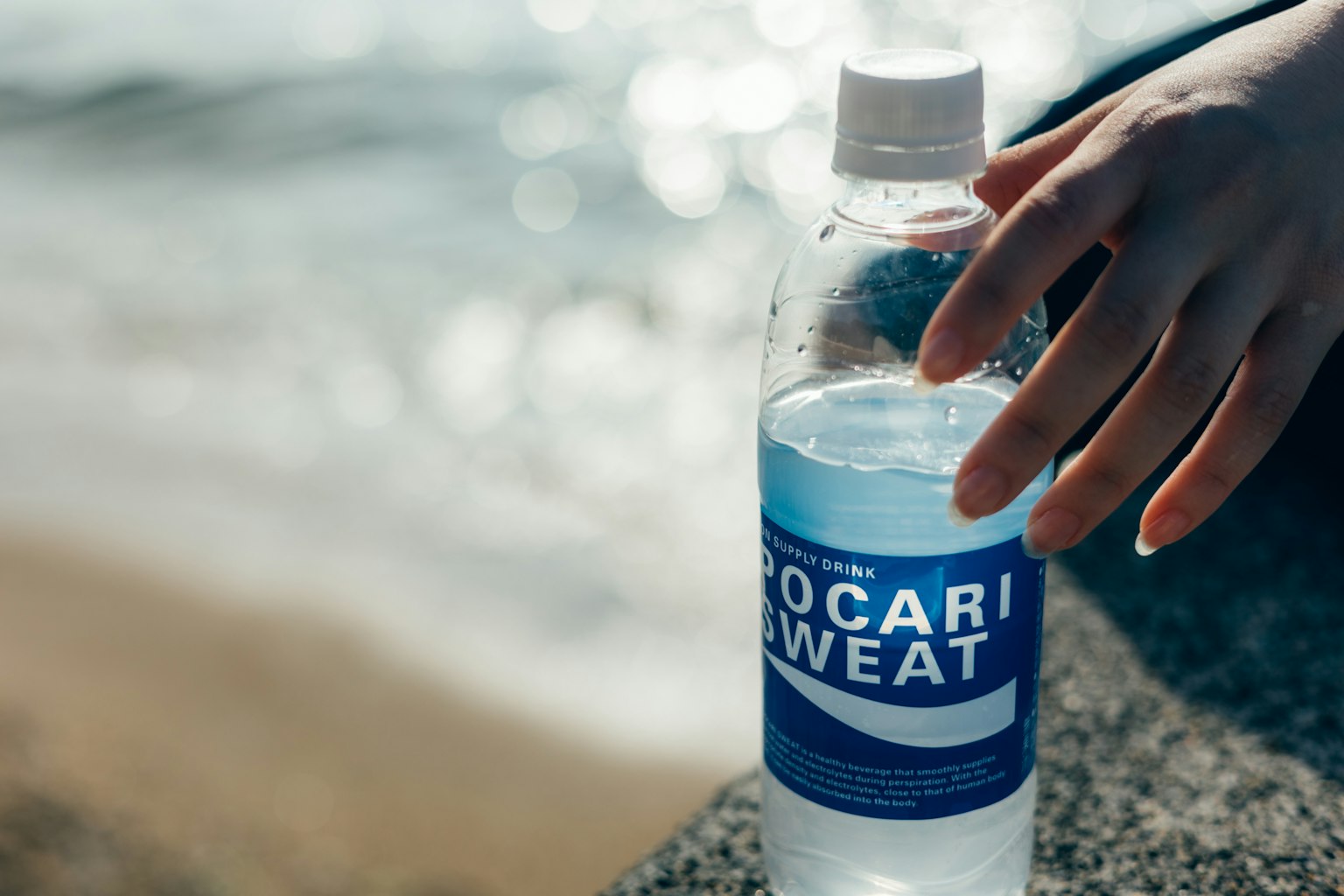 Hình ảnh chai nước thể thao gần đại dương với một bàn tay đang với tới