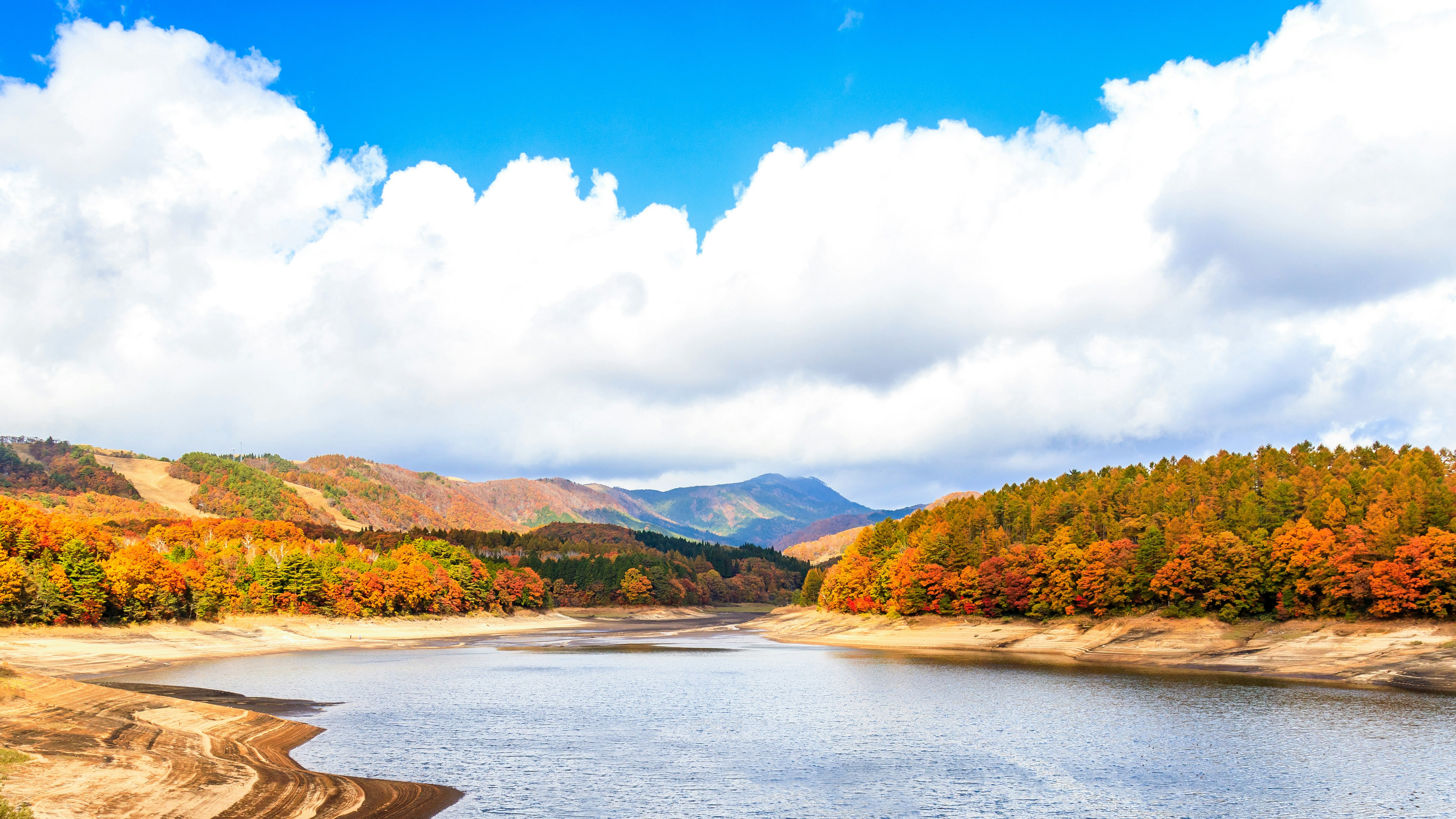 紅葉の山並みと湖の流れ、青空の下の風景