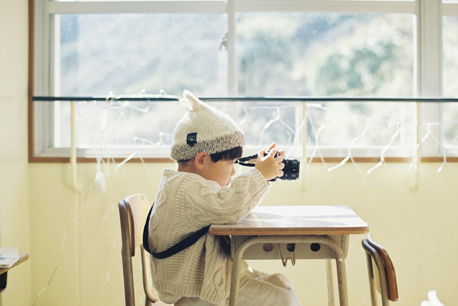 เด็กนั่งที่โต๊ะถือกล้องในห้องสว่าง