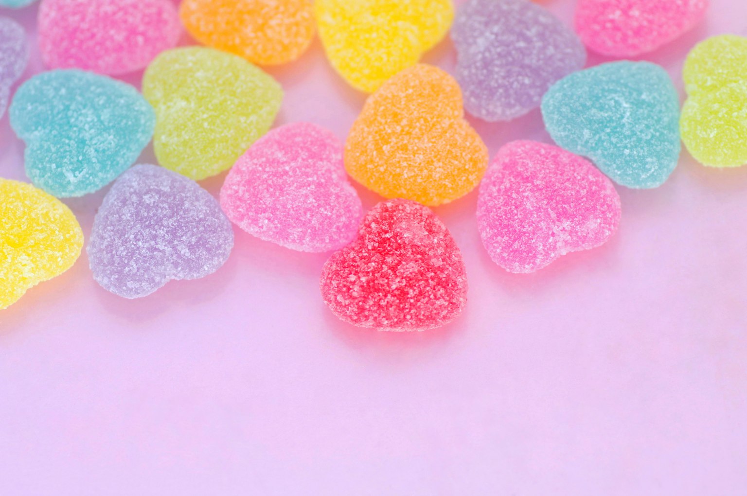 Bunte herzförmige Gummibärchen auf einem rosa Hintergrund verstreut