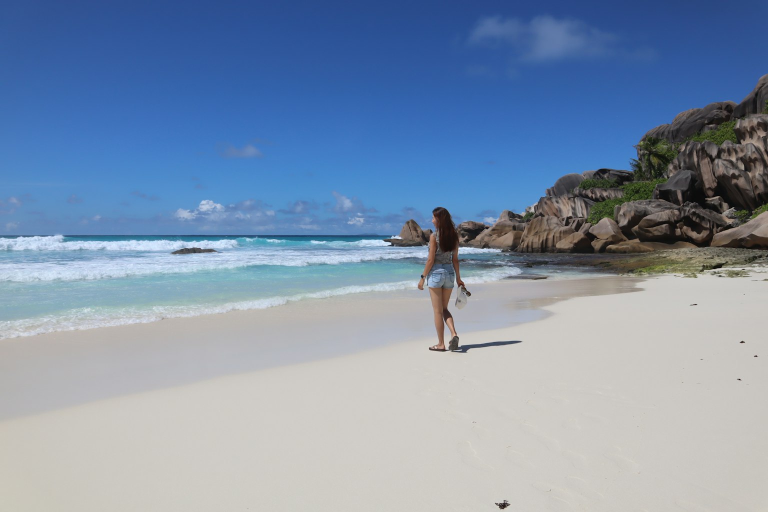 Une femme marchant sur une plage avec océan bleu et sable blanc