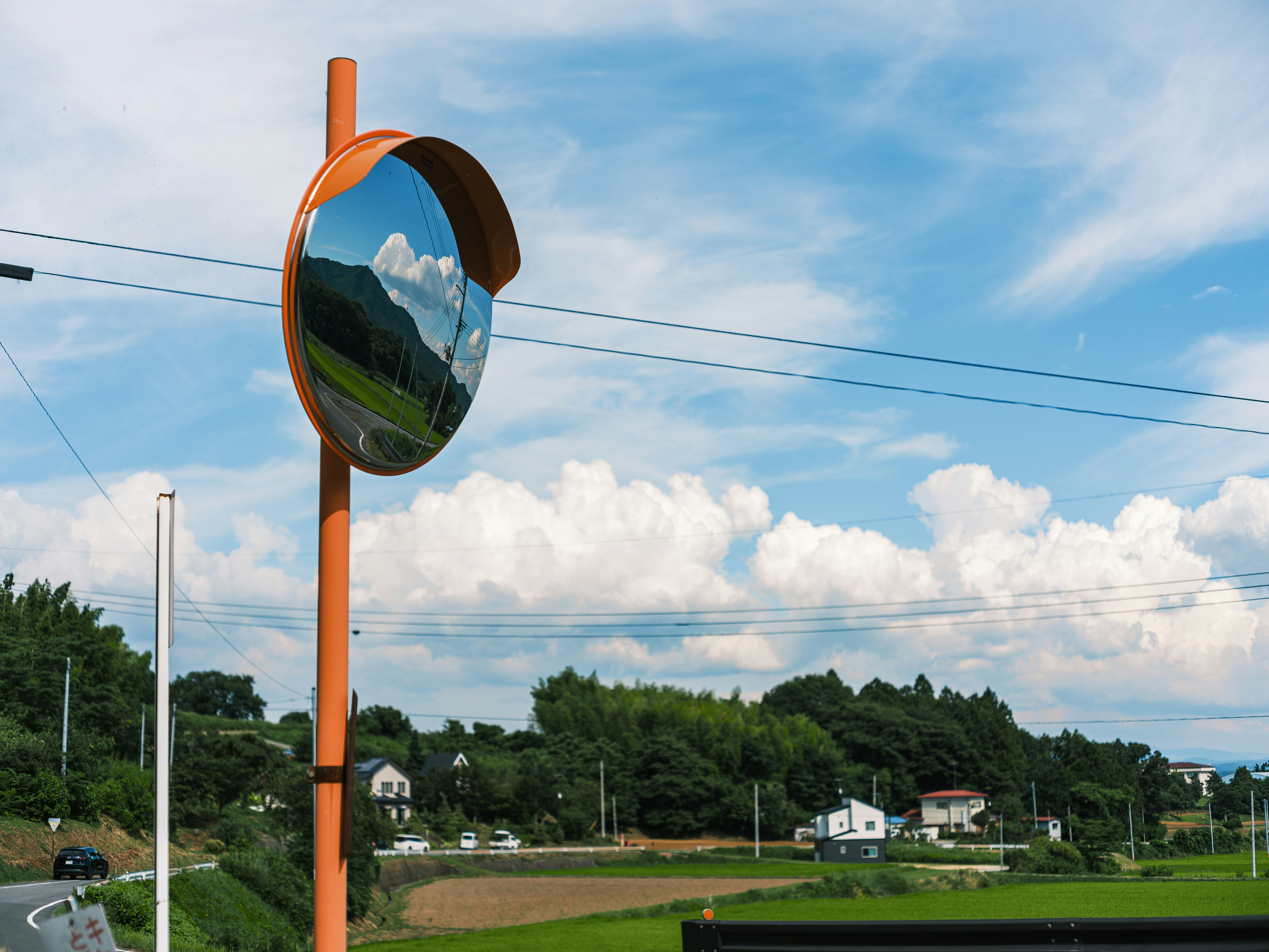 Landscape with a roadside convex mirror under a blue sky