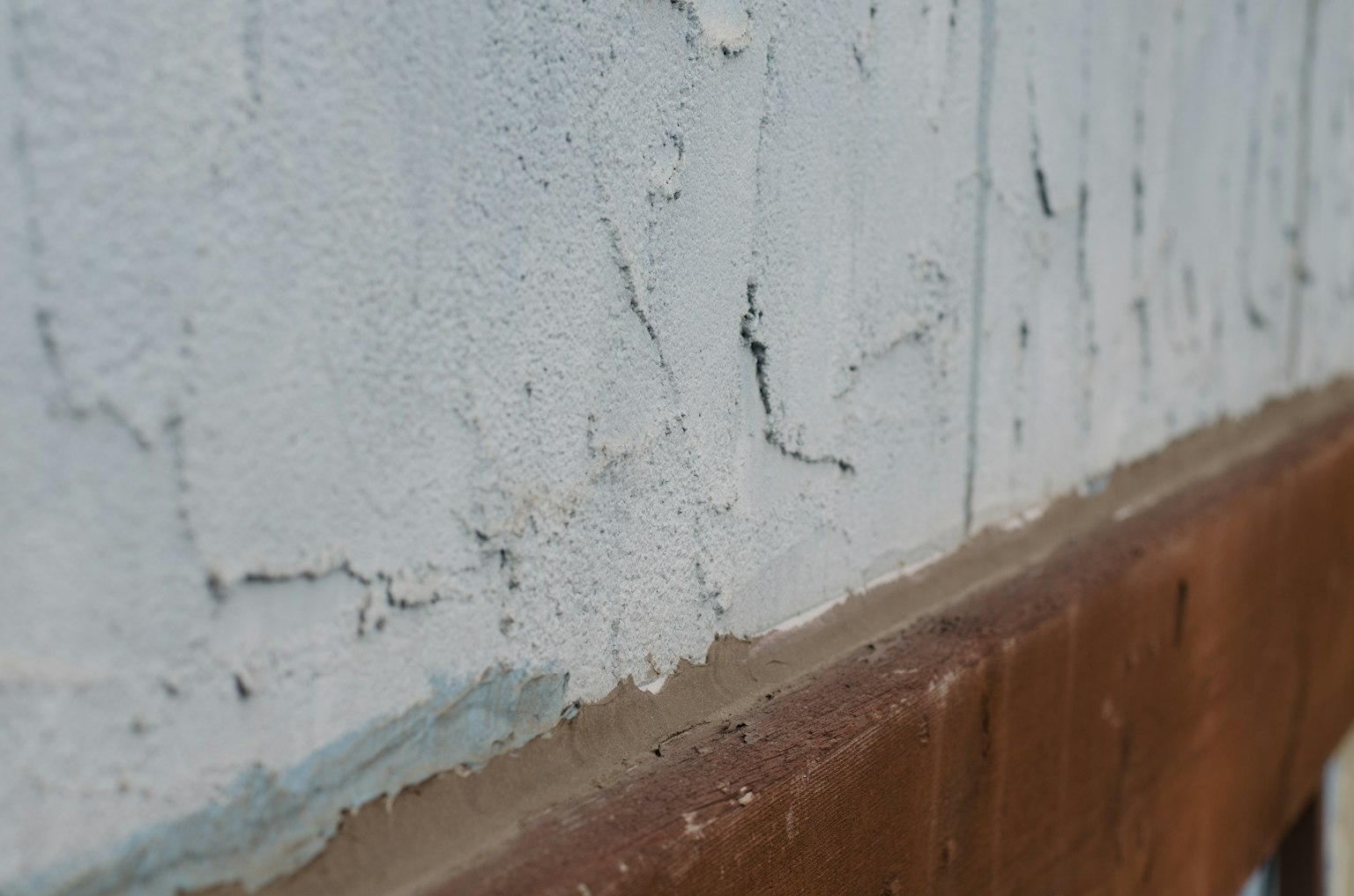Nahaufnahme einer weißen Wand mit Rissen und einem braunen Fundament