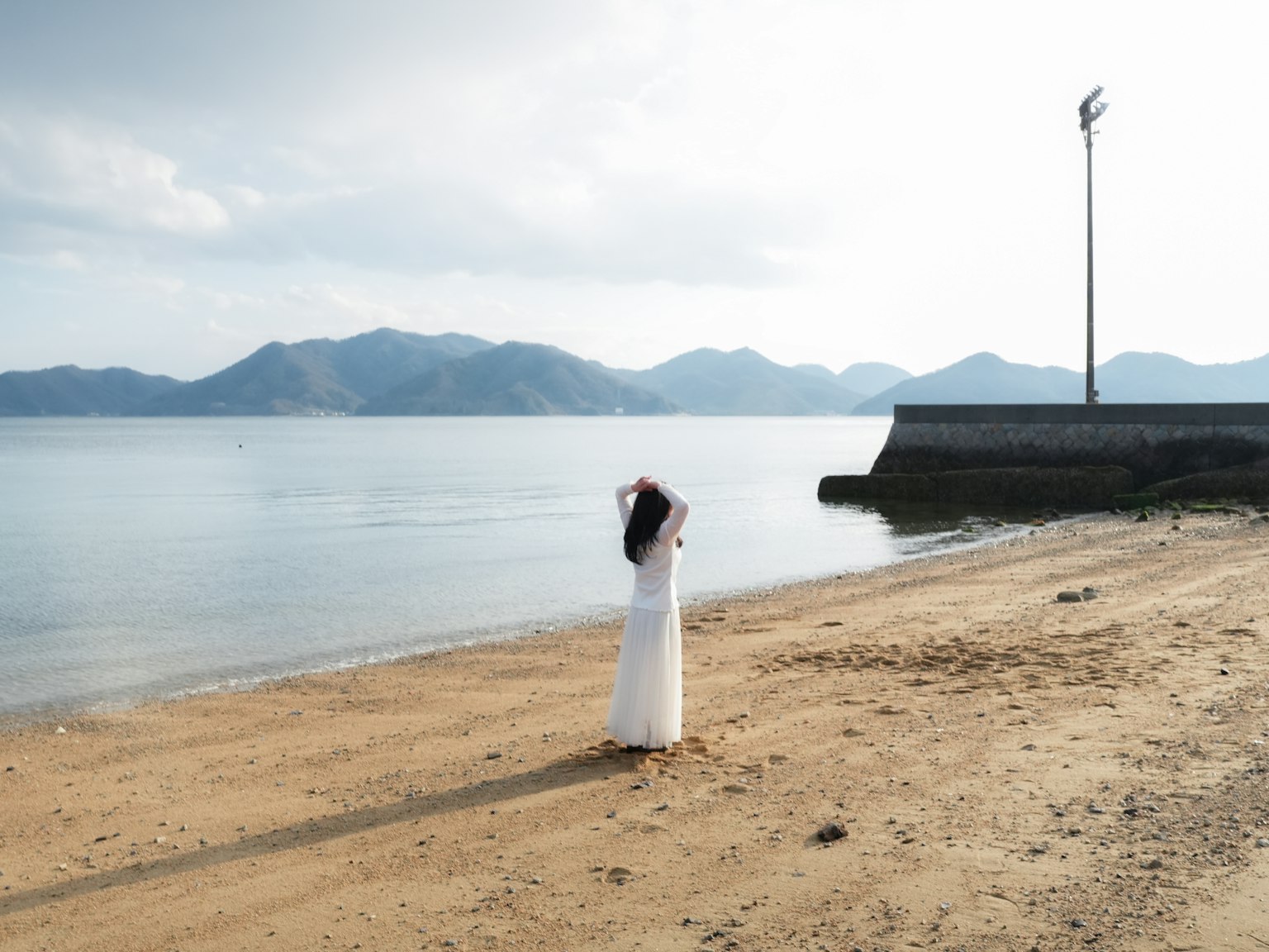 Một người phụ nữ trong chiếc váy trắng đứng trên bãi biển nhìn ra biển