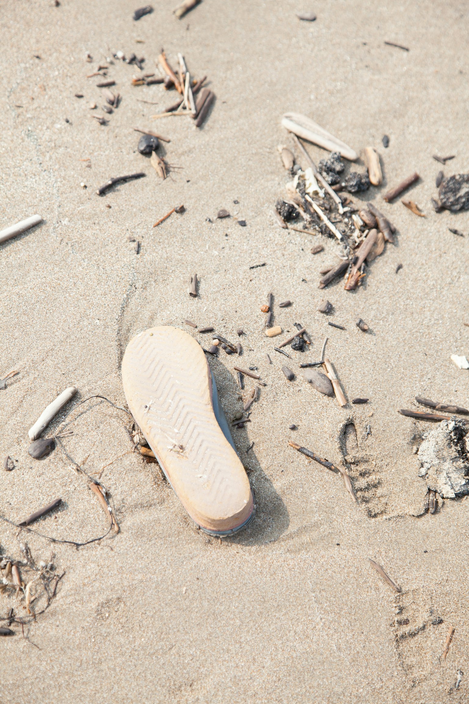 Weiße Schuhsohle am Sandstrand umgeben von kleinen Zweigen und Abfällen