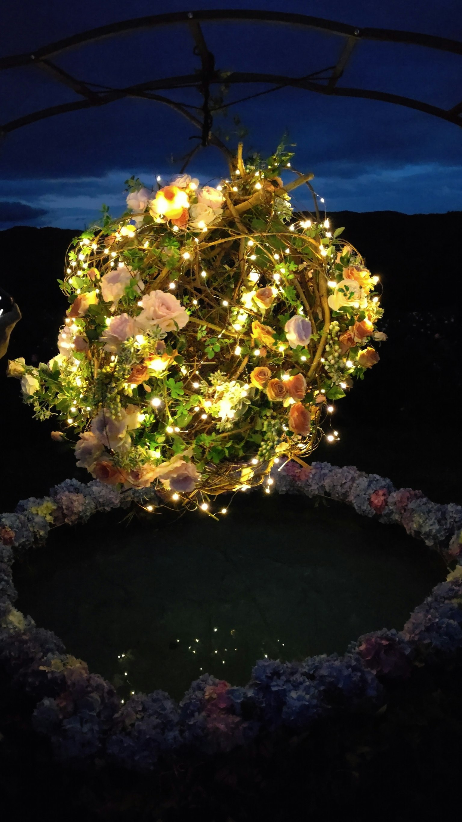 Orbe décoratif suspendu avec des fleurs et des lumières dans un ciel sombre