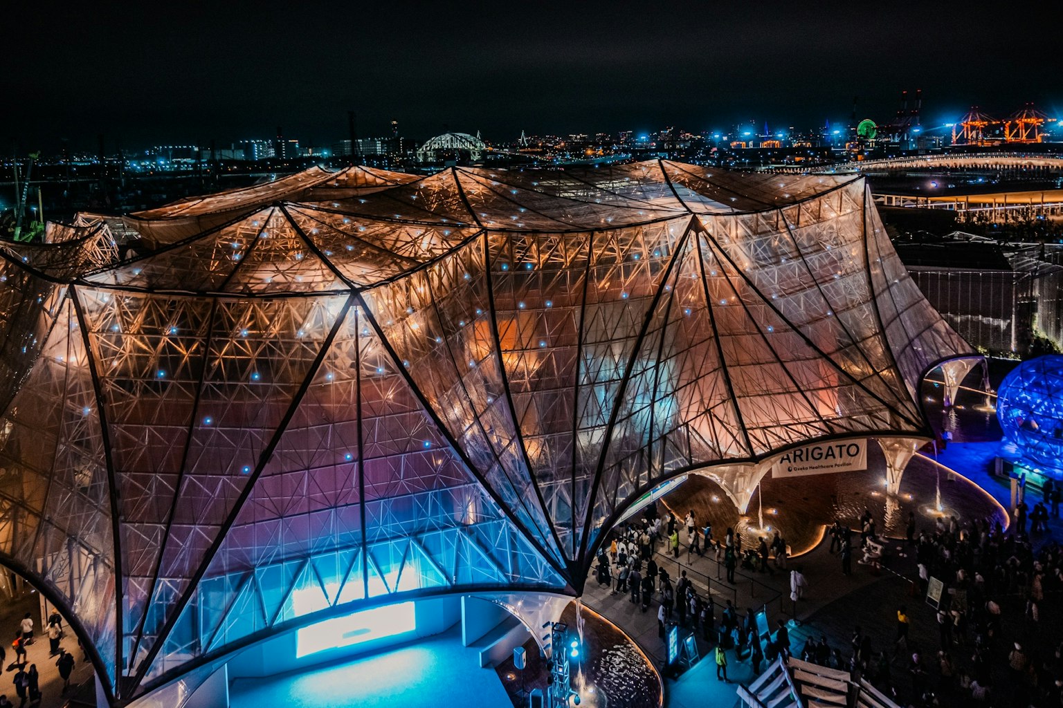 夜のエキスポ会場の近代的な建物の外観 光る装飾と多くの人々が集まる様子